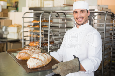 Happy baker holding tray of fresh bread