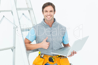 Repairman showing thumbs up sign while using laptop