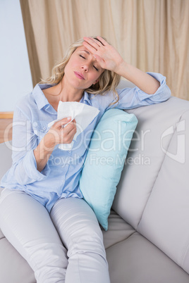 Sick blonde sitting on couch holding tissue