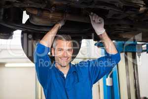 Mechanic smiling at the camera under car