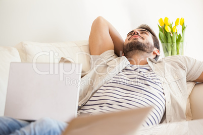 Hipster man using laptop lying on couch