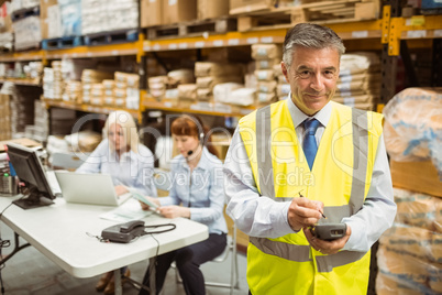 Smiling manager wearing yellow vest using handheld