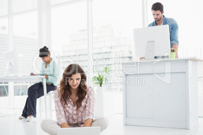 Cheerful businesswoman sitting on the floor using laptop