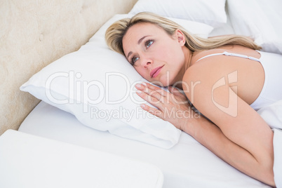 Thoughtful blonde woman lying in bed