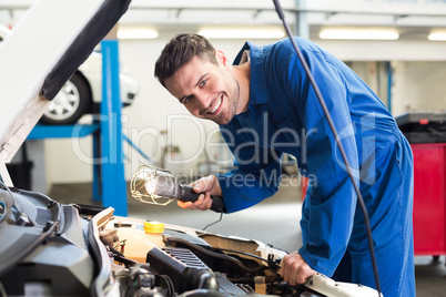 Mechanic examining under hood of car with torch