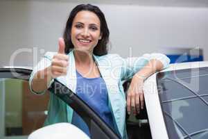 Smiling customer leaning on car while giving thumbs up