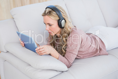 Blonde lying on couch listening music while using tablet
