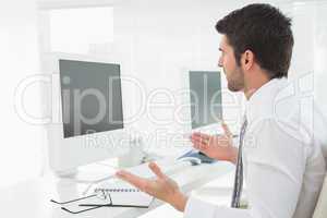 Unsmiling businessman gesturing in front of his computer