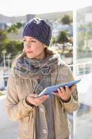 Thoughtful blonde in warm clothes using tablet