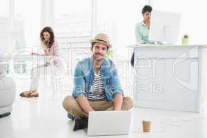 Smiling businessman sitting on the floor using laptop