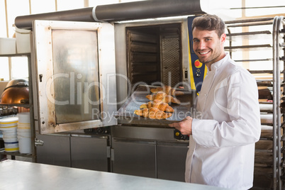 Smiling baker taking fresh croissants out of the oven