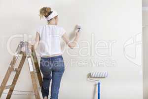 Frau streicht Wand auf Leiter