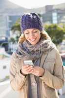 Smiling blonde in warm clothes text messaging