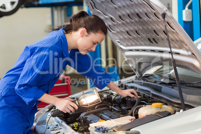 Mechanic examining under hood of car with torch