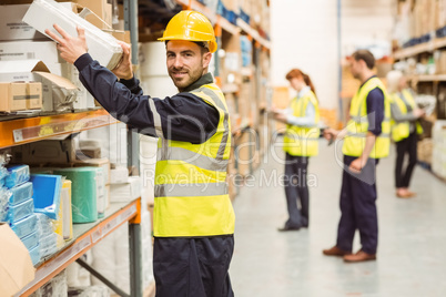 Smiling warehouse worker taking package in the shelf