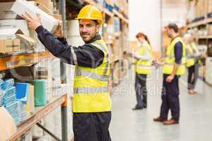 Smiling warehouse worker taking package in the shelf