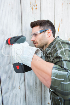 Carpenter using hand drill on wooden cabin