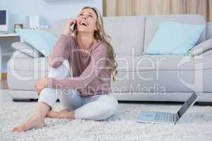 Happy blonde sitting on carpet phoning