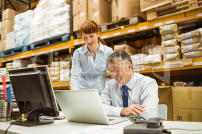 Warehouse management talking and looking at laptop