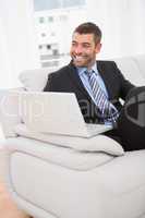 Smiling businessman on a sofa with a laptop