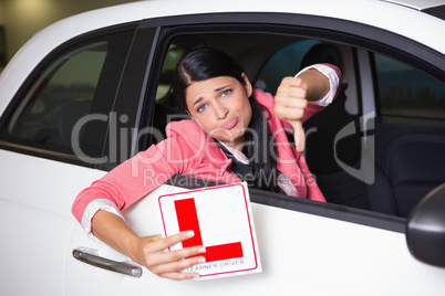 Woman gesturing thumbs down holding a learner driver sign