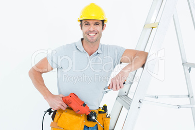 Technician holding drill machine while leaning on step ladder