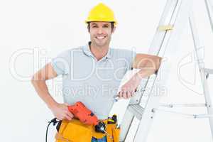 Technician holding drill machine while leaning on step ladder