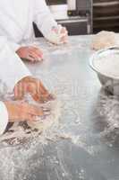 Close up of bakers kneading dough at counter
