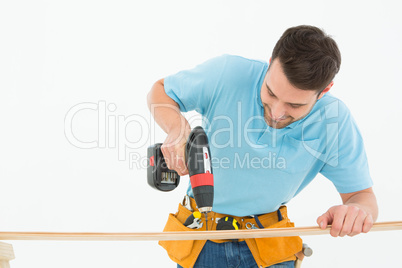 Construction worker using hand drill on wooden plank