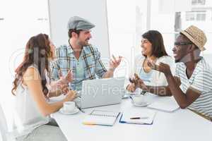 Smiling colleagues interacting and using laptop