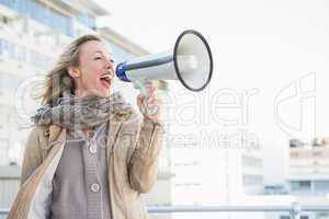 Happy blonde woman speaking on megaphone