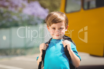 Cute pupil smiling at camera by the school bus