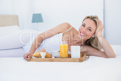 Smiling blonde lying and having breakfast in bed