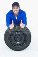 Mechanic leaning on tire while gesturing thumbs up