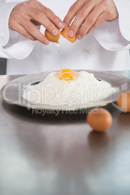 Close up of baker breaking eggs into flour