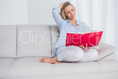 Calm blonde sitting on couch reading notebook