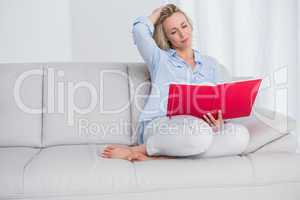 Calm blonde sitting on couch reading notebook