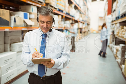 Smiling warehouse manager writing on clipboard