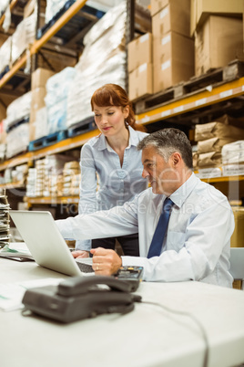 Warehouse management talking and looking at laptop