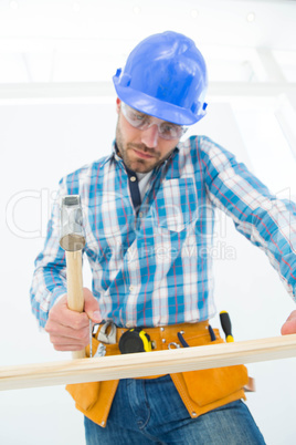 Carpenter hitting nail on wooden plank