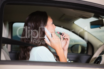 Woman using mirror to put on lipstick while on the phone