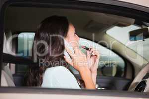 Woman using mirror to put on lipstick while on the phone