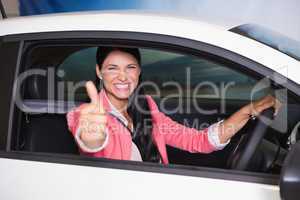 Smiling woman driving while giving thumbs up