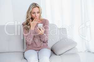 Surprised blonde sitting on couch reading message