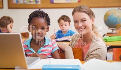 Cute pupil using computer with teacher