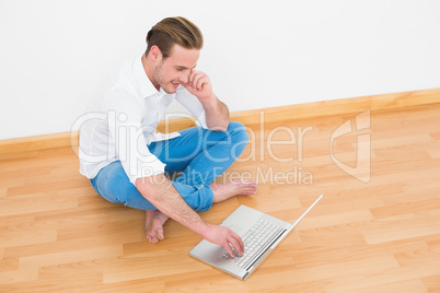 Casual man sitting on floor using laptop at home