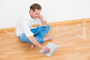 Casual man sitting on floor using laptop at home