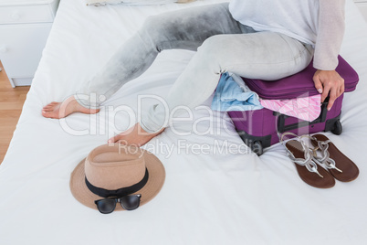 Woman sitting on baggage to close it