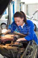 Mechanic examining under hood of car with torch