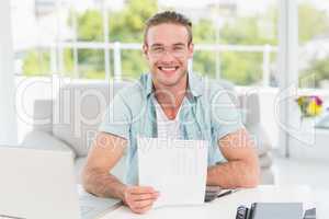 Happy businessman sitting at his desk holding document